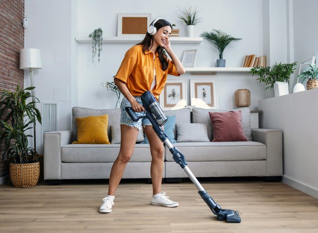 Shot of young happy woman listening and dancing to music while cleaning the living room floor with a vaccum cleaner