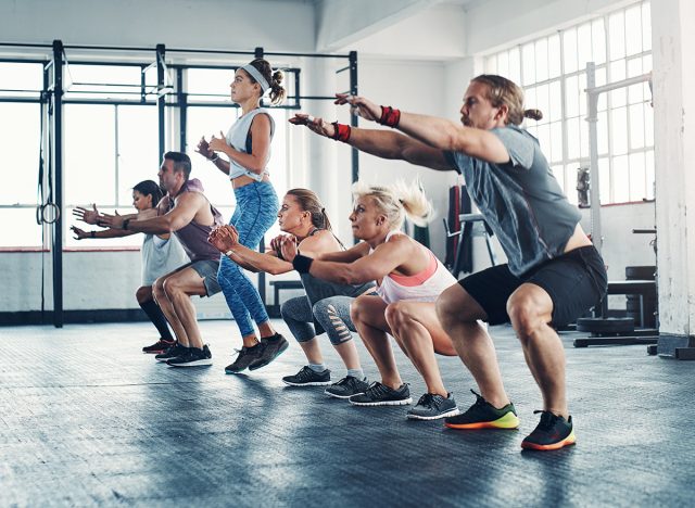 Fitness, personal trainer and group squat for exercise, healthy workout and training in gym class. Athlete, man and women team together for power challenge, commitment or strong muscle at club