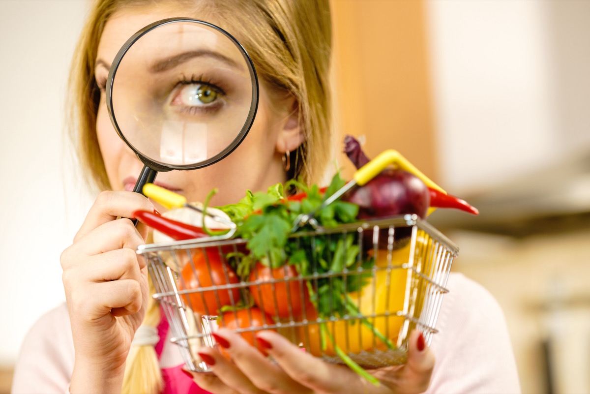 Woman using magnifying glass loupe, investigating shopping basket with many colorful vegetables. Healthy eating lifestyle, nutrients vegetarian food, searching for pesticides and chemicals.