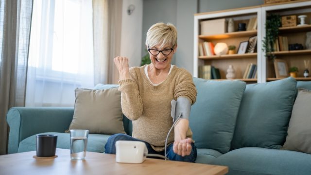 One woman senior caucasian female use blood pressure device on hand to check health results while sit at home real people health care concept healthy celebrate good results smile