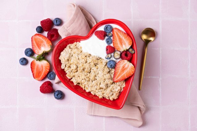 Oatmeal porridge with berry and yogurt in red bowl in the heart shape, top view. Oat flakes healthy breakfast meal. Clean eating, dieting, healthy food